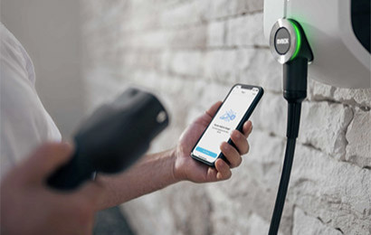 EVBox Elvi mounted to a wall with a person holding onto  mobile phone in one hand and the plug in another.
