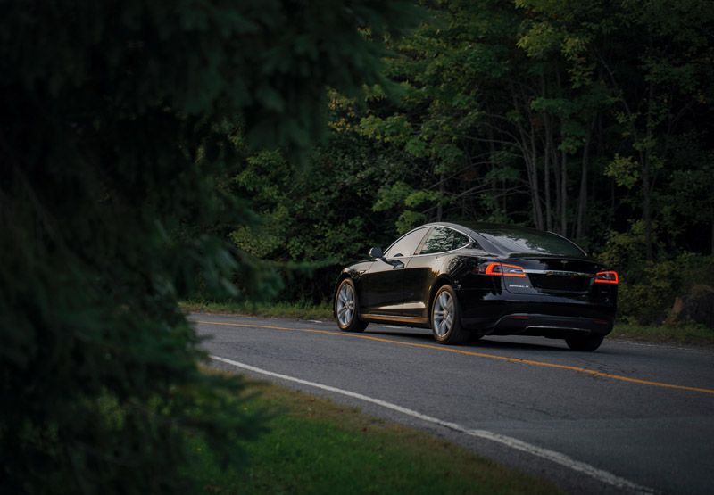 tesla elektrische auto op verharde weg in een bos tijdens zonsondergang