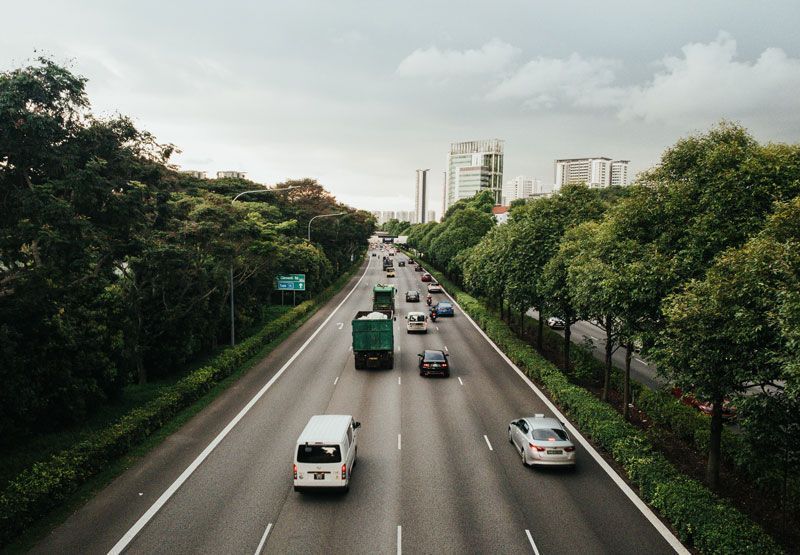 An areal shot of a busy high-way road with a line of trees next to it.
