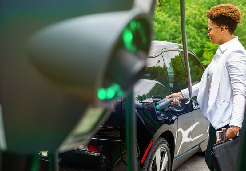 A woman wearing casual business attire that's plugging an EVBox Business Line charger into her electric vehicle