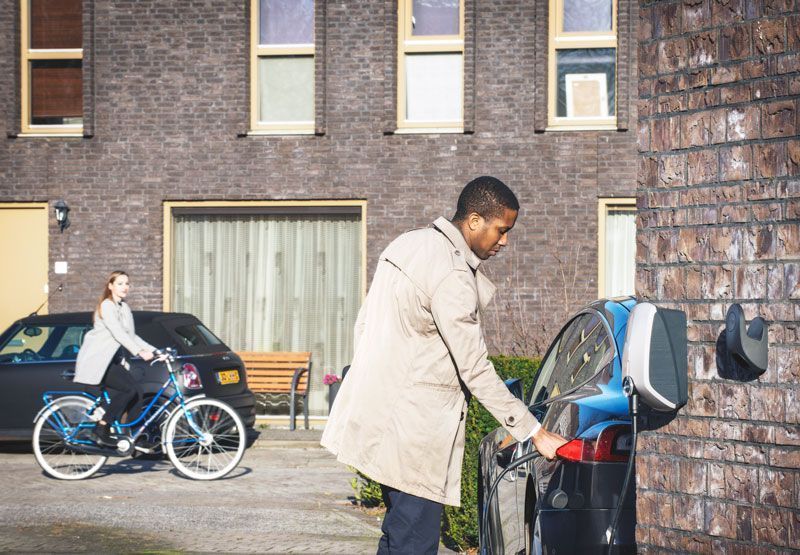 man laadt zijn Tesla elektrische auto thuis op de oprit met de EVBox Elvi laadpaal