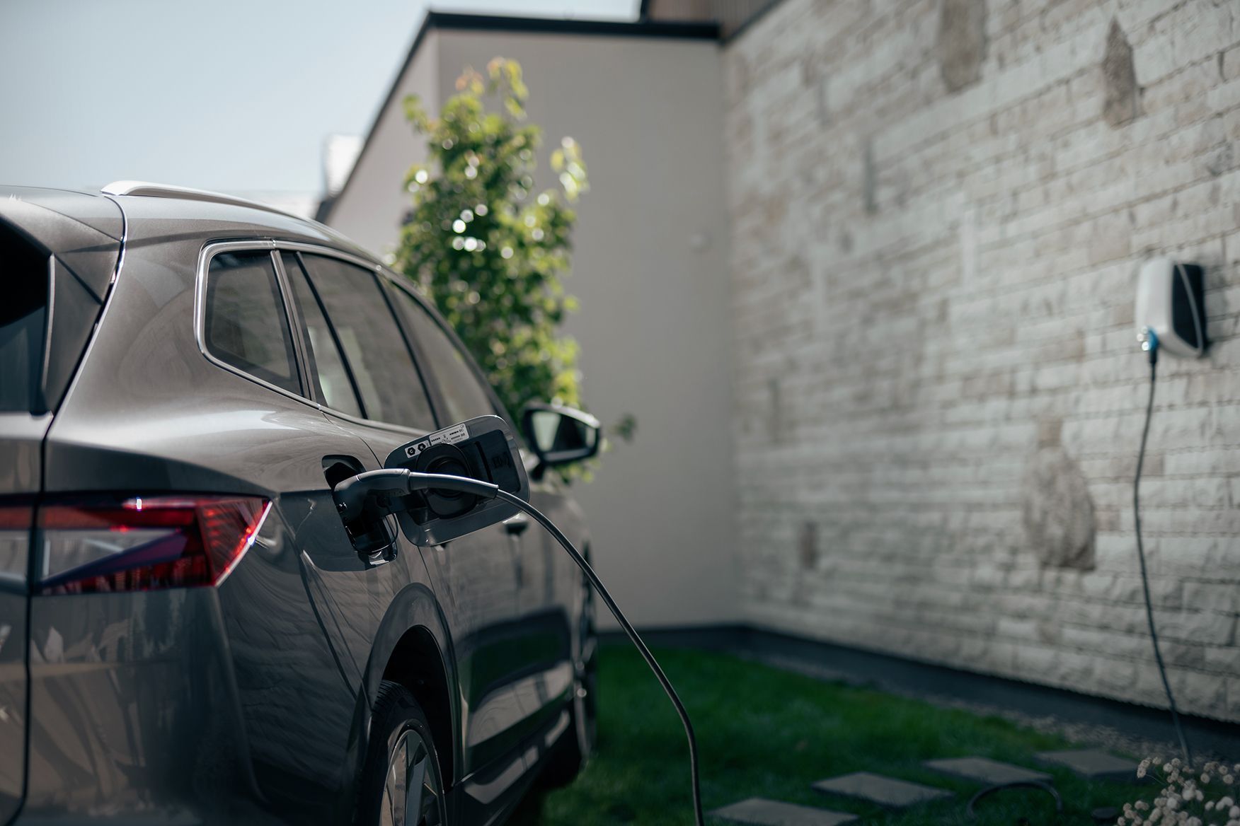 A car is parked outside of the house while it's connected and charging to the EVBox Elvi charging station placed on the house's brick wall.