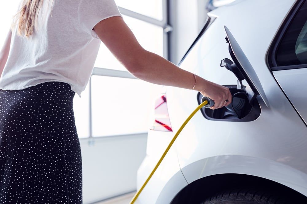 A lady plugging in her charging cable in her garage.