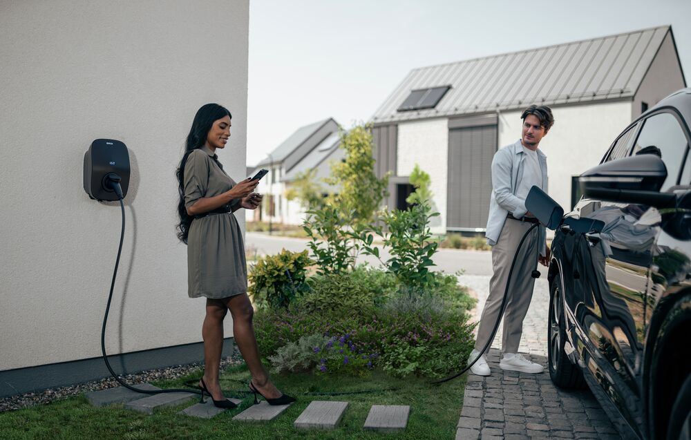 Woman looking at phone while man uses EVBox Livo to charge electric car.