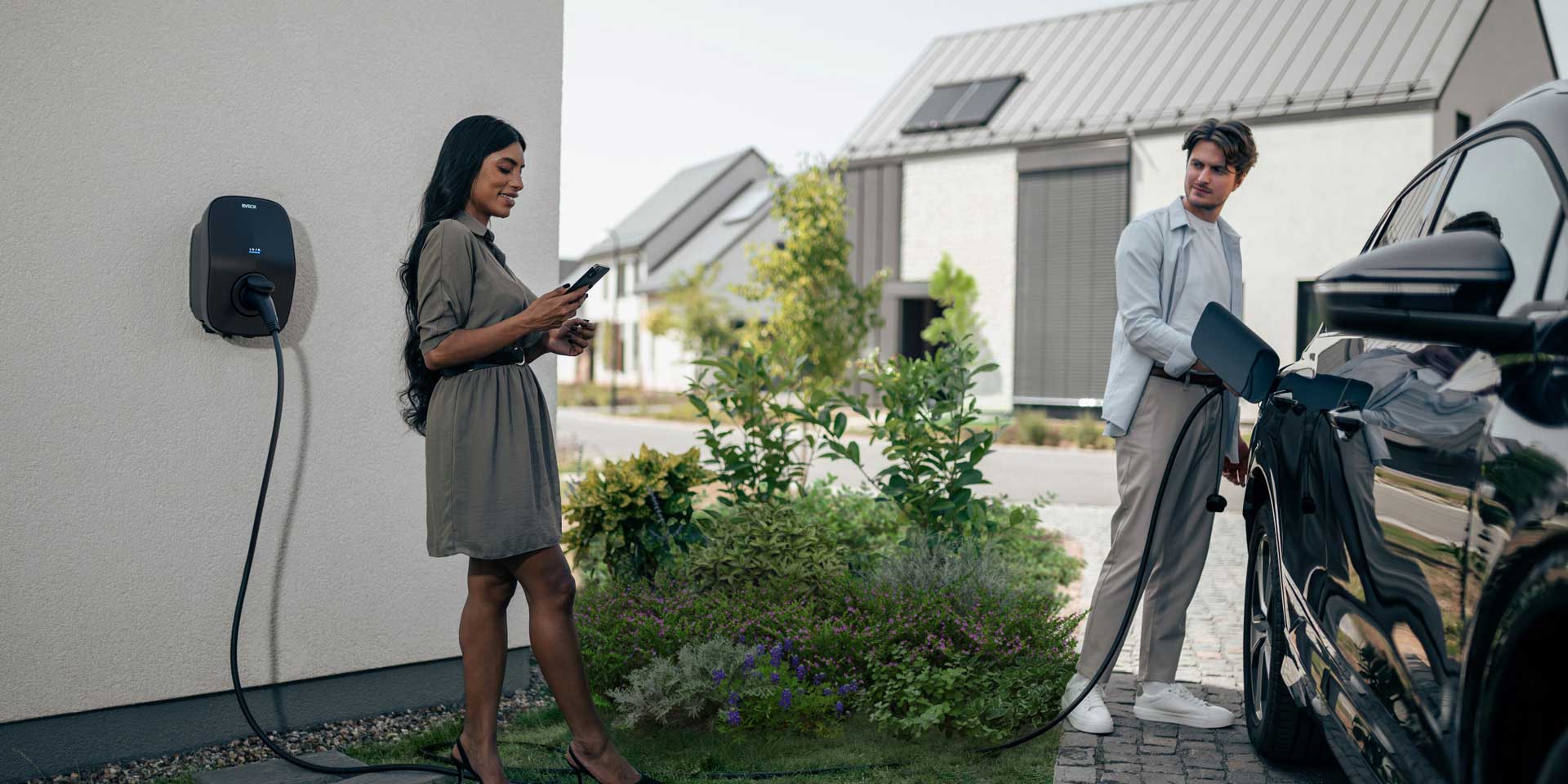 a man and woman next to EVBox Livo that's mounted to their wall and charging their car.