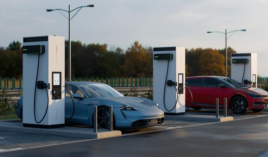 Two modern EVs charging at a DC fast charging hub near a highway.