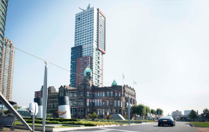 A skyline showing a modern skyscraper behind a more traditional building, some trees and a patch of green.