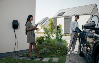 A couple standing next to their EV while it's charging in their driveway