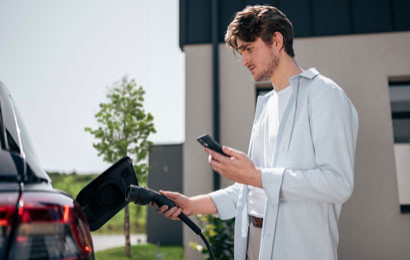 A man holding a phone and a charging cable next to his EV