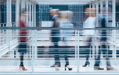 Employees walking across an internal bridge in a corporate environment. The photograph is taken with a slowed shutter speed to capture the movement.