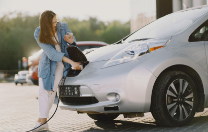 A modern office worker charging her electric vehicle whilst checking important business updates.