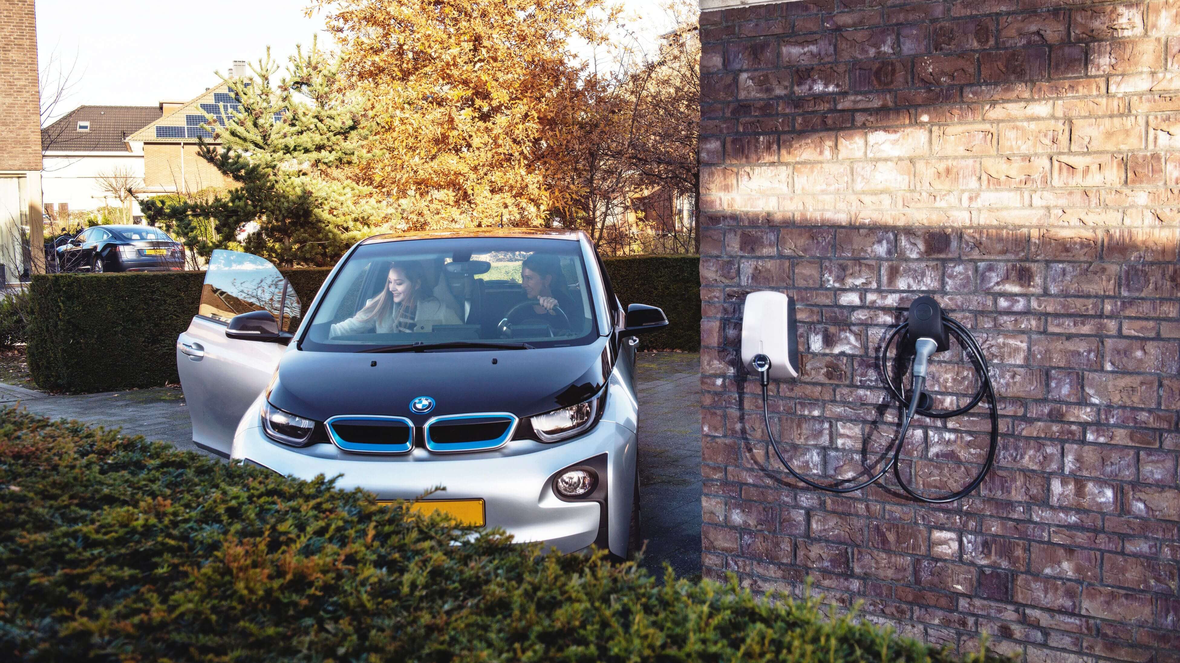 twee vrouwen in bmw i3 elektrische auto op de oprit voor het huis met een EVBox Elvi laadpaal